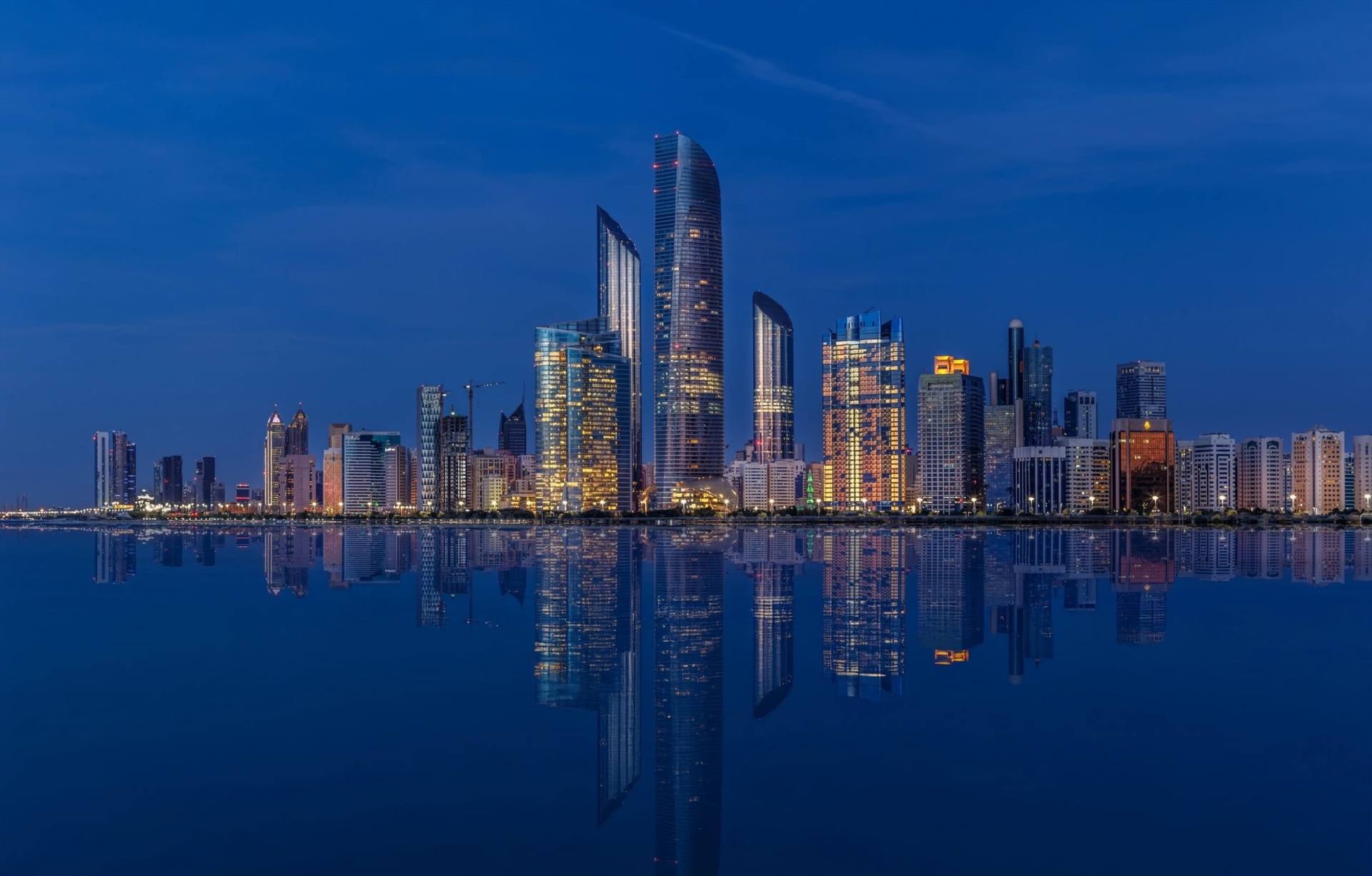 City skyline at dusk with lit towers reflected in calm water